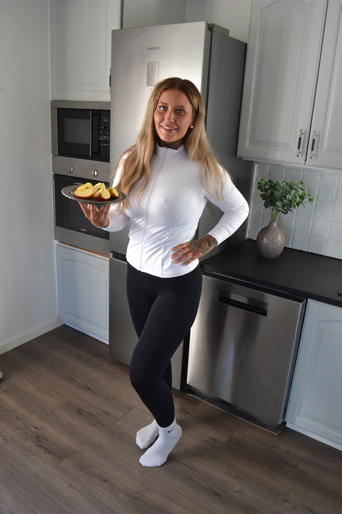 Coachen står i sitt kök och håller en tallrik med skivad äpple.